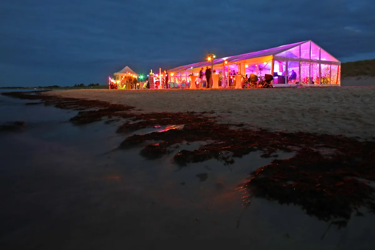 Beleuchtetes Glaszelt am Strand aus der Ferne